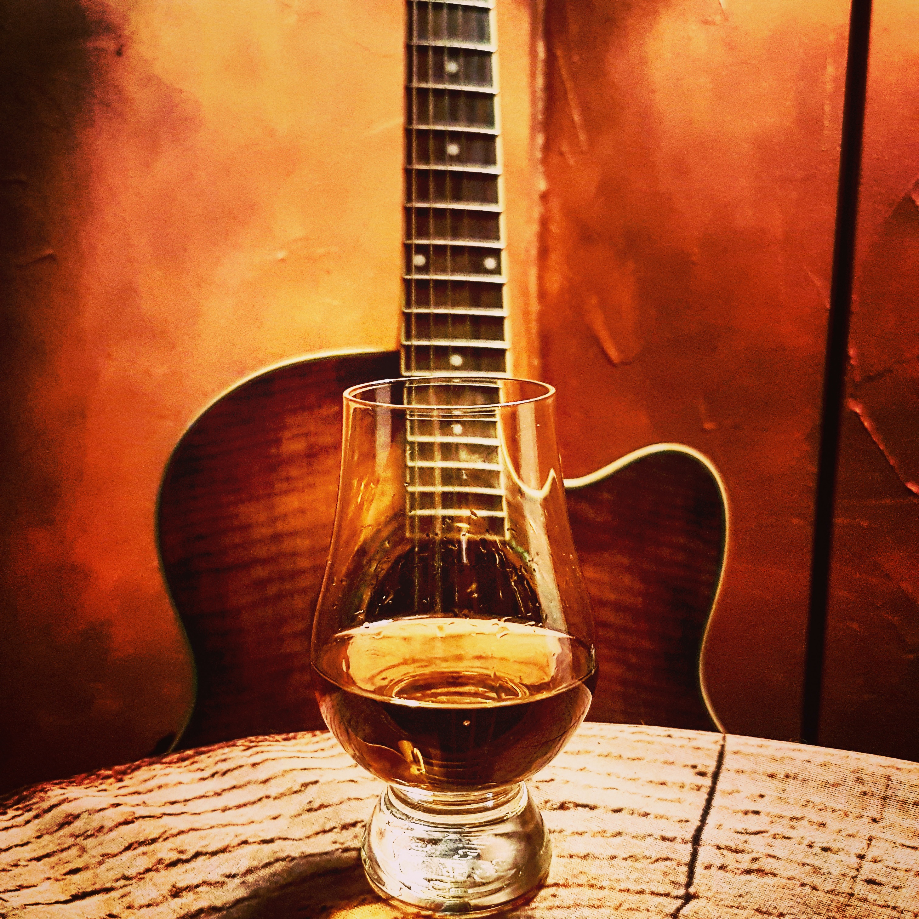 Ein Glas Whisky mit einer Gitarre im Hintergrund.