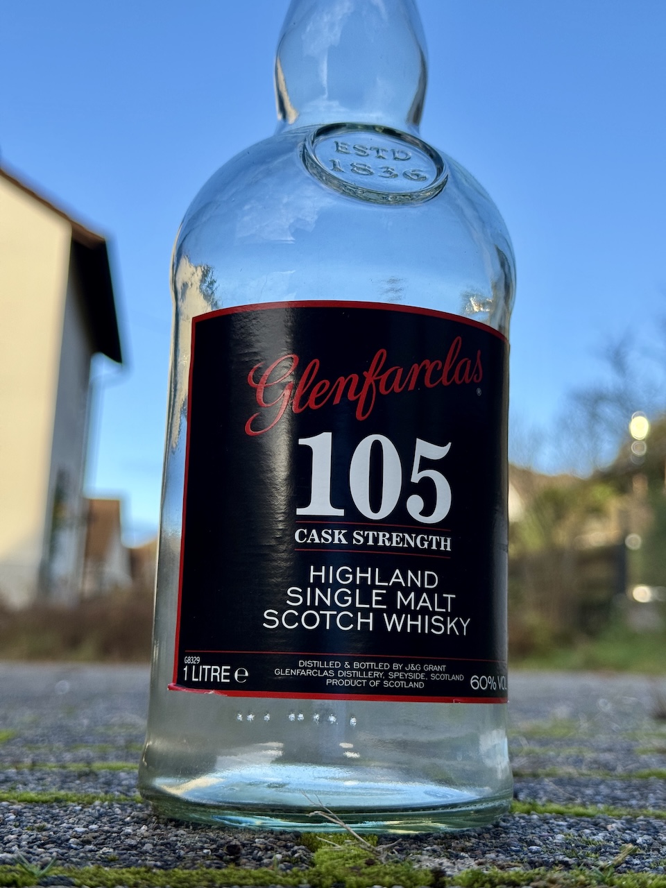 Leere Glenfarclas 105 Cask Strength Flasche auf dem Boden im Freien, fotografiert aus niedriger Perspektive.