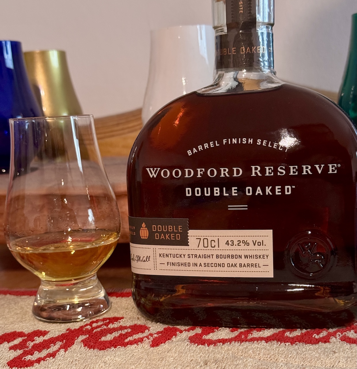 Woodford Reserve Double Oaked Bourbonflasche und Whiskyglas auf einer Tischunterlage, Hintergrund leicht unscharf.